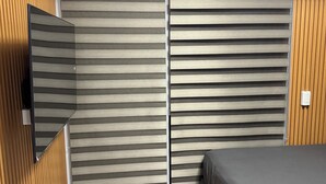 A bedroom with a bed, a TV mounted on the wall, and a sliding door. - Studio Unit with Balcony in Manila (Manila)