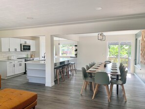 A modern kitchen with white cabinets, a central island, and a dining area with a long table and green chairs.