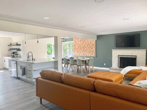 A modern living room with a sofa, a dining area with chairs, a kitchen with a sink, and a fireplace.