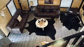 Um quarto com painéis de madeira, um sofá de couro marrom, um tapete de couro de vaca preto e branco, uma mesinha redonda e um quadro na parede.