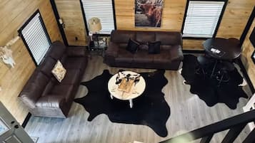 Une pièce aux murs lambrissés, avec un canapé en cuir marron, un tapis en peau de vache noir et blanc, une petite table ronde et un tableau encadré accroché au mur.