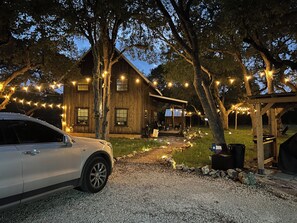Un chalet rustique avec une allée en gravier, des guirlandes lumineuses et un espace salon extérieur.