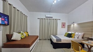 A compact hotel room with a bed, a sofa, a small table, a chair, and a TV mounted on the wall.