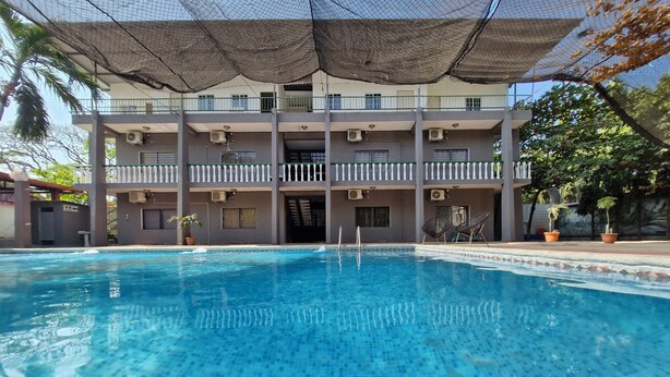 A swimming pool with clear blue water, surrounded by a covered area with a balcony.