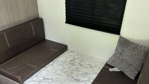 Ein kompaktes Wohnmobil-Interieur mit Schlafsofa, kleinem Tisch und einem Fenster mit Jalousien.