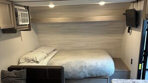 Ein kompakter Wohnraum in einem Wohnmobil mit einem Bett, einer kleinen Küchenzeile und einer Sitzecke.