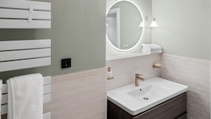 Une salle de bain avec un lavabo blanc, un meuble-lavabo en bois foncé, un porte-serviettes blanc et un miroir rond avec éclairage intégré.