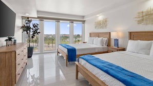 A modern hotel room with two beds, a wooden dresser, a potted plant, and a view through large windows. - The Zen Side at Solare Tower (South Padre Island)