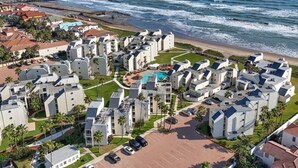 A coastal residential area with modern buildings, a central swimming pool, and a pier in the background. - The Zen Side at Solare Tower (South Padre Island)