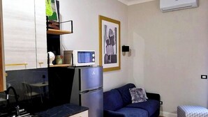 A compact kitchen with a microwave, refrigerator, and a small dining area. There is a sofa and a cushioned bench in the living area. - LeChiavidiCasa (Roma)