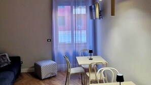 A modern living room with a sofa, a dining table with chairs, a small ottoman, and a large window with curtains. - LeChiavidiCasa (Roma)