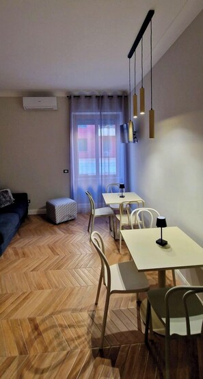 A modern living room with a sofa, a dining table with chairs, a small ottoman, and a large window with curtains. - LeChiavidiCasa (Roma)