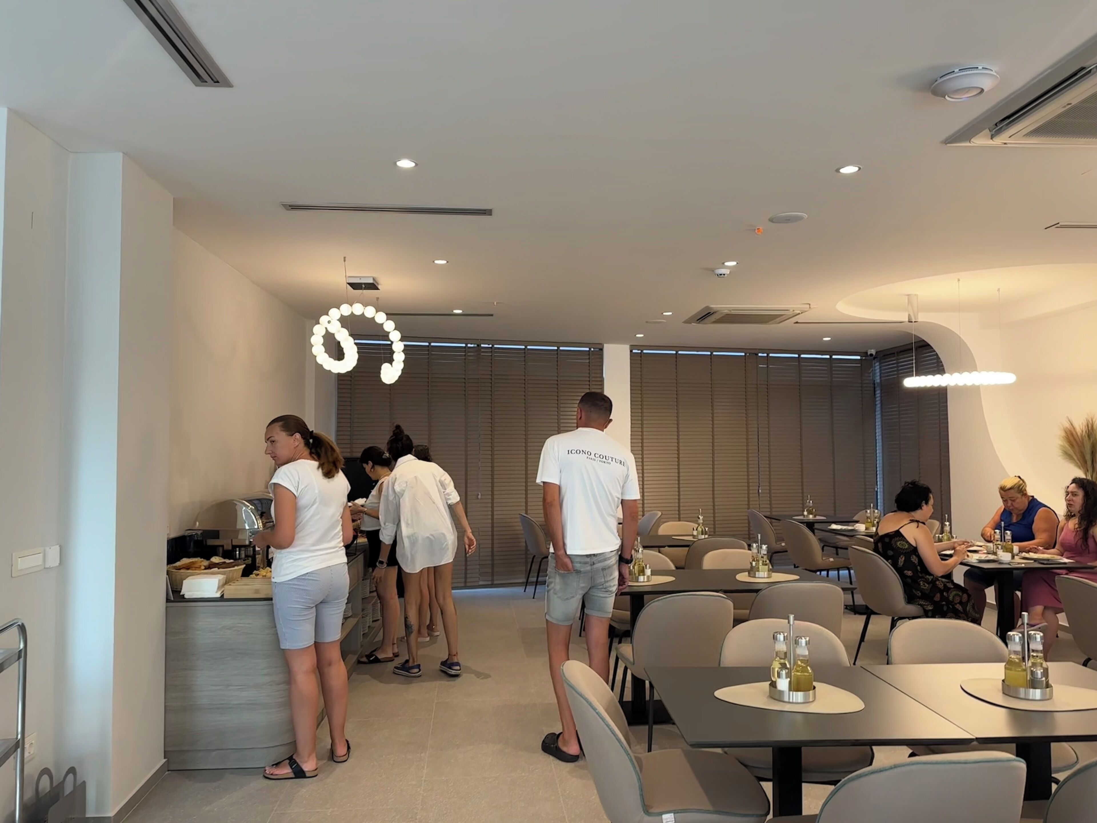 A modern dining area with tables and chairs, a counter with food items, and a ceiling with recessed lighting.