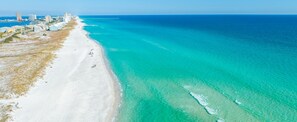 An aerial view of a beach with clear turquoise waters, a sandy shore, and buildings in the background. - Newly Renovated! Heated Pool, Beach Gear, Pet Friendly, Gulf Views, Beach Access (Pensacola Beach)