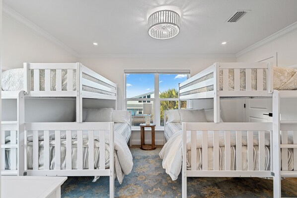 A room with bunk beds, a chandelier, a small table, and a view through a window.