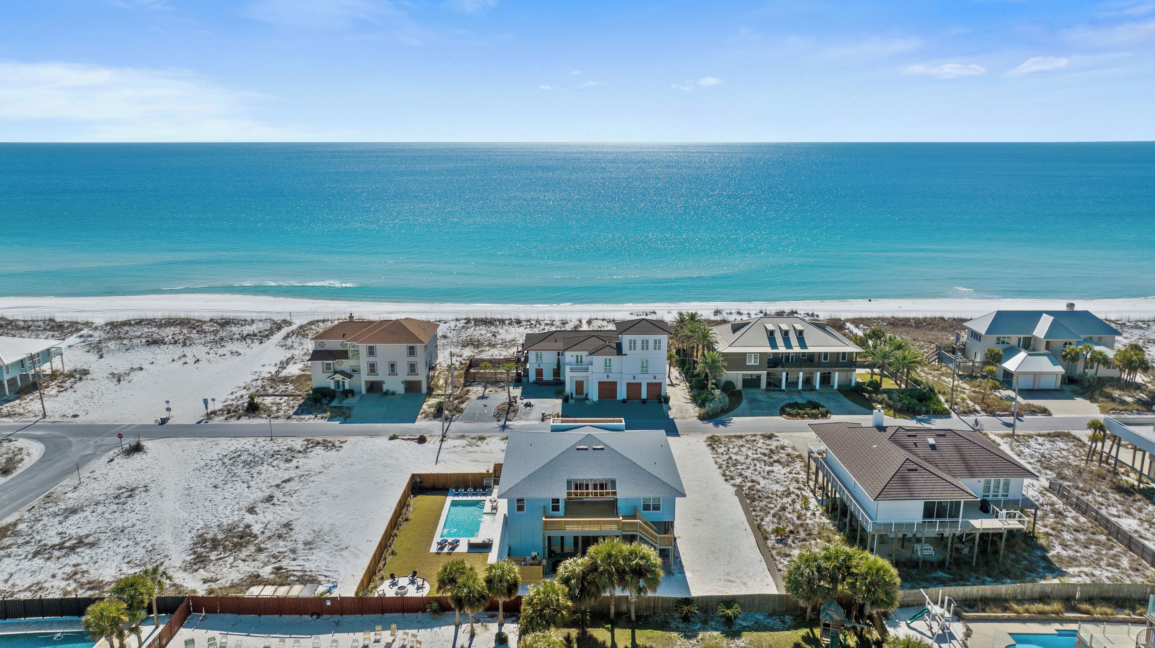 A coastal residential area with multiple houses, a swimming pool, and a beach in the background.