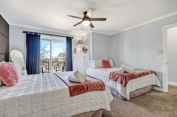 A bedroom with two beds, a ceiling fan, a window with curtains, and a view of the outdoors.