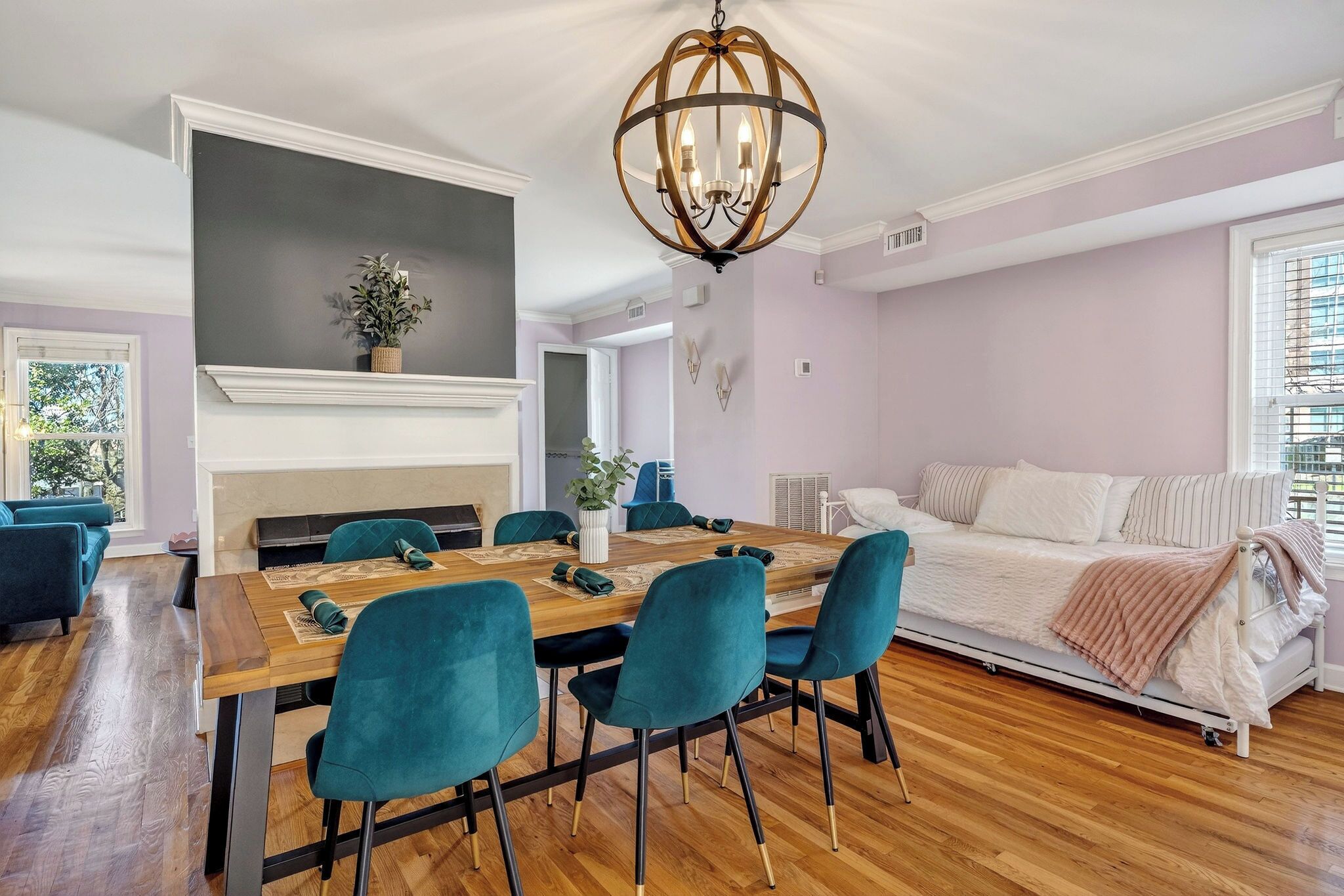 Un coin repas avec une table en bois et des chaises de couleur turquoise, une cheminée et un canapé, le tout dans une pièce dotée de planchers en bois et d’une grande fenêtre.