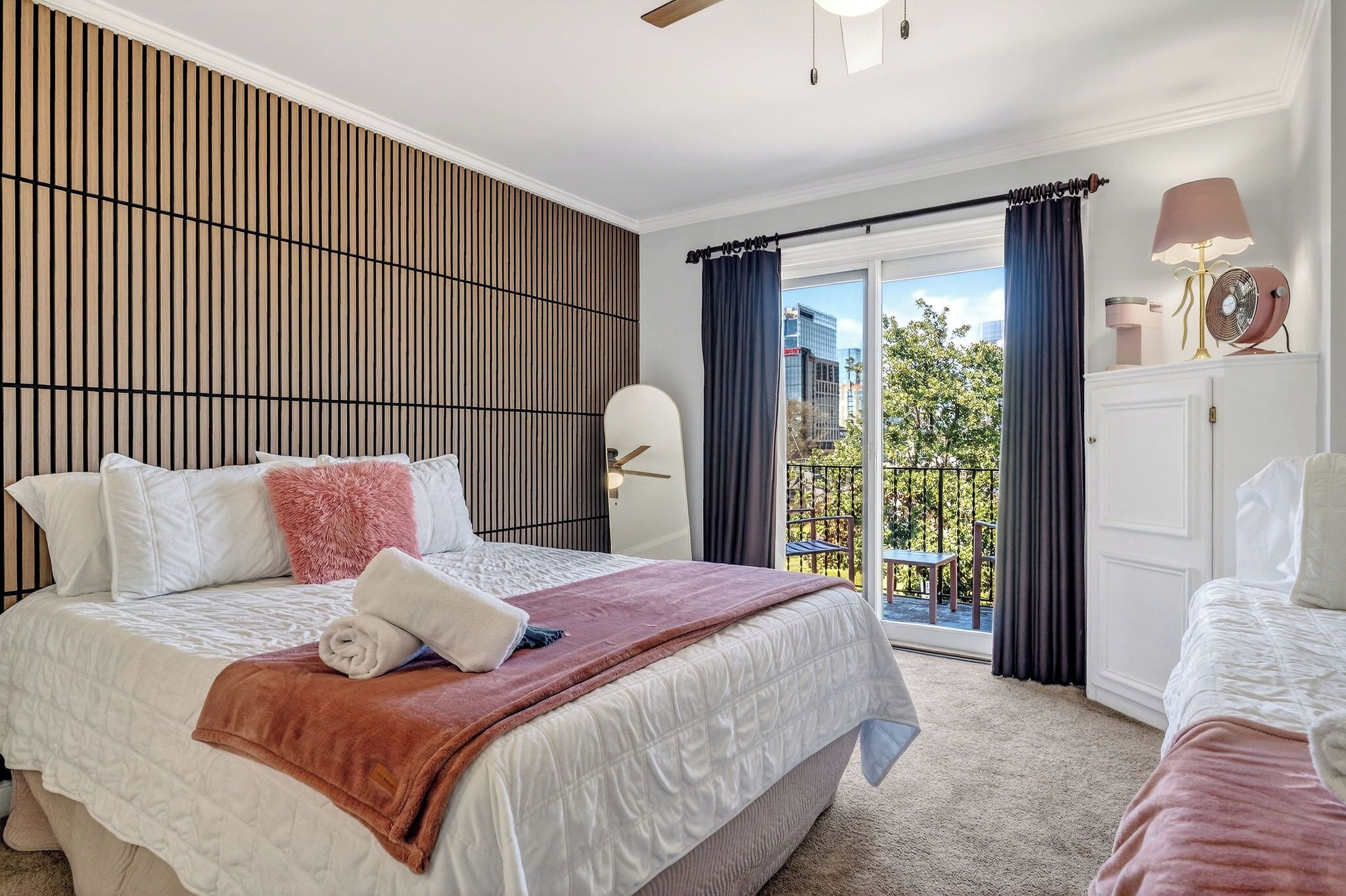 Une chambre d’hôtel avec un lit, une table de chevet, une lampe, un ventilateur et une vue sur l’extérieur.