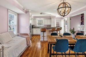 A modern kitchen with white cabinets, a wooden dining table, and blue chairs. - See Fireworks from the Balcony! ParkFree (Nashville)