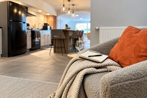 A cozy living area with a sofa, a notebook, and a pen, leading to a kitchen with modern appliances and a dining area.