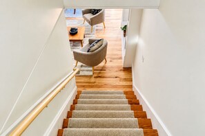 Una escalera conduce a una sala de estar con piso de madera, un sofá y una mesa de centro.