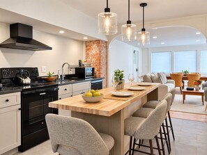 A modern kitchen with a central island, black appliances, and a brick accent wall.