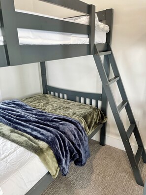 Una cama litera con escalera, una manta verde y una almohada blanca.