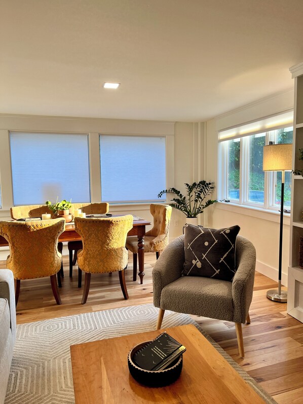 Una sala de estar con sofá, mesa de centro, mesa de comedor con sillas y estantería.