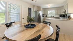 A modern kitchen with white cabinets, a central island, and a dining area with a wooden table and chairs. - Dockside Dreams-**Best Game/Movie Room at the Lake (Winchester)