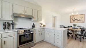 A modern kitchen with white cabinetry, a stainless steel stove, and a dining area with a wooden table and chairs. - Dockside Dreams-**Best Game/Movie Room at the Lake (Winchester)
