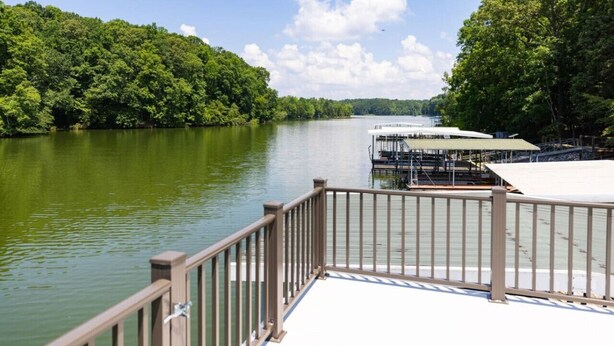 A riverside dock with a wooden railing, a covered seating area, and a view of a forested area across the water. - Dockside Dreams-**Best Game/Movie Room at the Lake (Winchester)