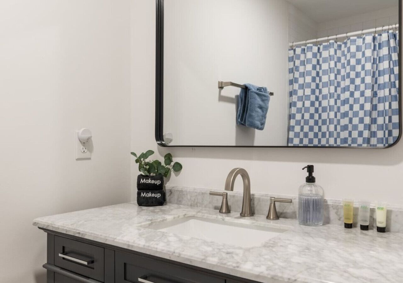A bathroom with a marble sink, a mirror, a towel rack, a blue and white checkered shower curtain, and a potted plant labeled "Makeup Makeup".