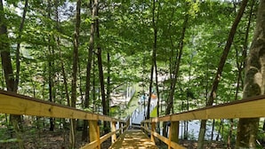 A wooden bridge in a forested area with a view of a building in the distance. - Dockside Dreams-**Best Game/Movie Room at the Lake (Winchester)