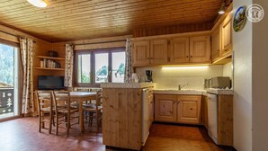 Interior de una cabaña de madera con cocina, comedor y un ventanal grande.
