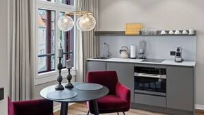 A modern kitchen with a dining area, including a round table, red chairs, and pendant lights.