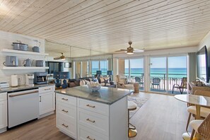 A spacious kitchen with white cabinetry and a large island, a dining area with a round table, and a balcony with a view of the ocean. - Crystal Beach with views (Destin)