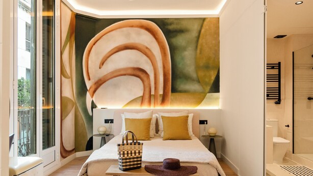 Une chambre moderne avec une grande fresque murale abstraite, un lit avec une tête de lit en bois, une table de chevet et un luminaire suspendu.