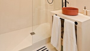 Une salle de bain moderne avec une douche à parois de verre, un miroir rond et un meuble-lavabo beige doté d’un lavabo rond.