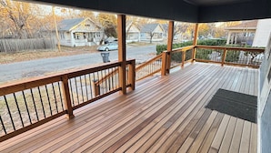 A wooden deck with railings, a covered area, and a view of houses and a street.