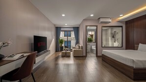 A modern hotel room with a TV displaying 'Netflix', a desk with a chair, a sofa, a bed, and a bathroom visible through an open door. - T P Villa (Da Nang)