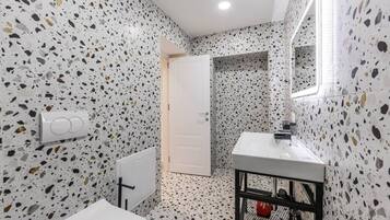 A bathroom with terrazzo flooring, a white sink, a mirror, and a door leading to another room.