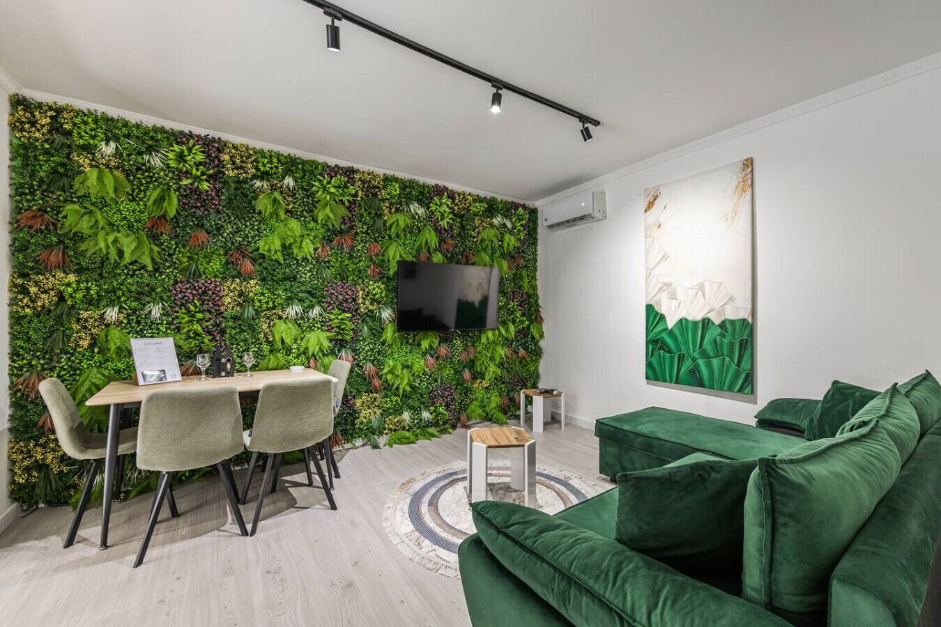 A modern living space with a green wall, a dining area, a sofa, and a TV mounted on the wall.