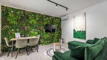 A modern living space with a green wall, a dining area, a sofa, and a TV mounted on the wall.