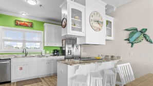 A kitchen with white cabinets, a central island with stools, a clock, and a decorative turtle wall art.