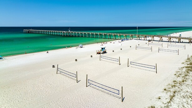 A beach with a long pier extending into the ocean, sandy beach, and volleyball nets.