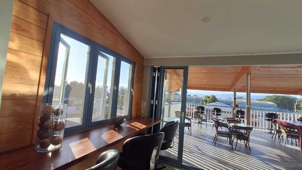 Una habitación moderna con detalles de madera, un comedor con una mesa larga y sillas, y un balcón con mobiliario exterior.