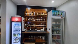 Una zona de bar con estantes llenos de botellas y un refrigerador repleto de bebidas.