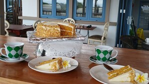 Comedor con una mesa de madera dispuesta para dos personas, mostrando un pastel y dos tazas con platillos a cuadros verdes y blancos.