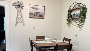 A dining area with a wooden table, chairs, a windmill decoration, a framed picture, and a shelf with plants. - Charming 2-bedroom apartment with WiFi, AC in Wabash. Great location (Wabash)